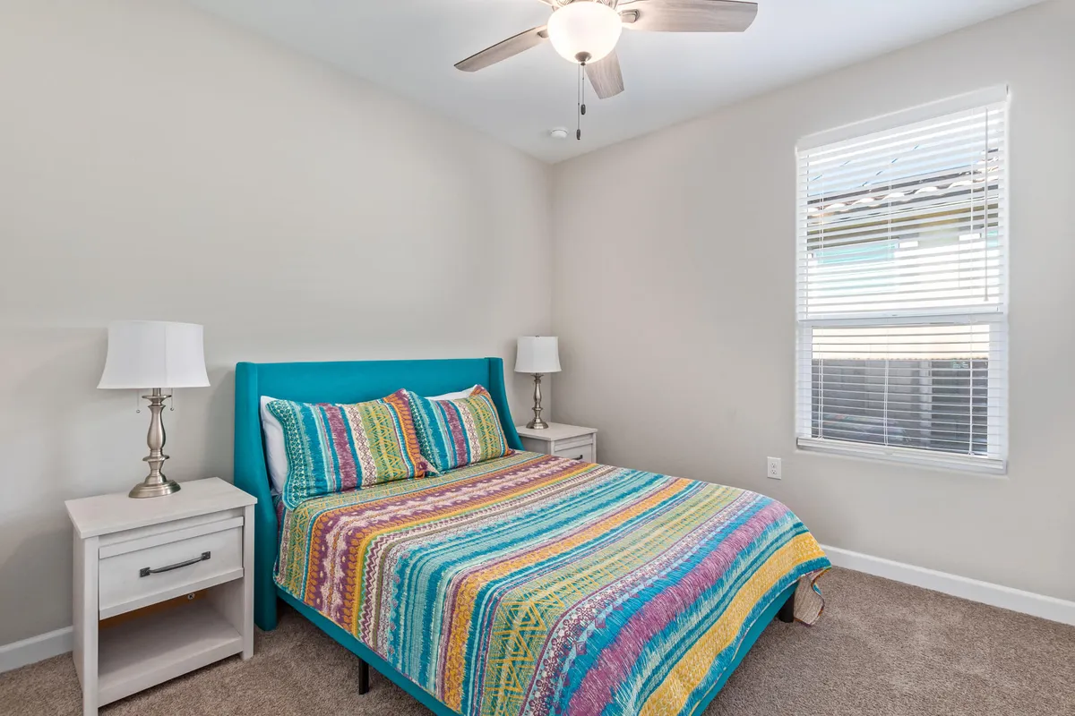 A cheerful bedroom highlighted by a colorful blue headboard, vibrant bedding, and nightstands with lamps. Sunlight gently filters through the window, creating a cozy and uplifting mood.