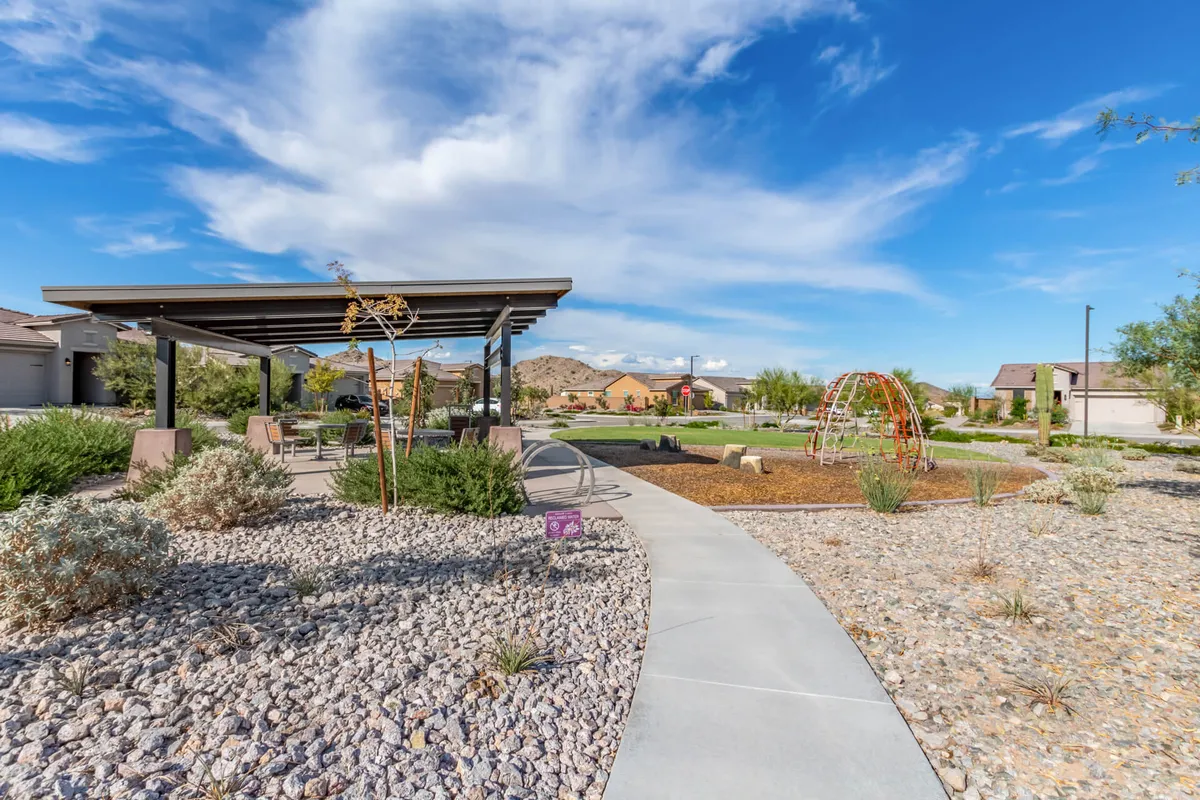 A lively neighborhood park featuring a modern playground structure under a pergola, landscaped gardens, and a wide pathway leading into the space. Children can be seen playing while families gather at shaded picnic tables, creating an atmosphere of community and fun.