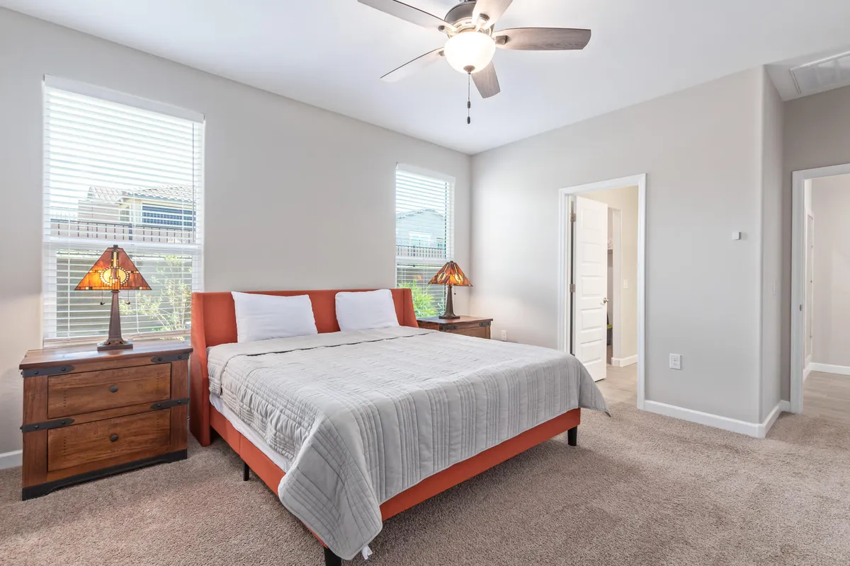 A serene bedroom featuring a comfortable bed with plush linens, matching nightstands, soft lamps, and windows that allow for natural light. The atmosphere is calm, inviting relaxation and restful sleep.