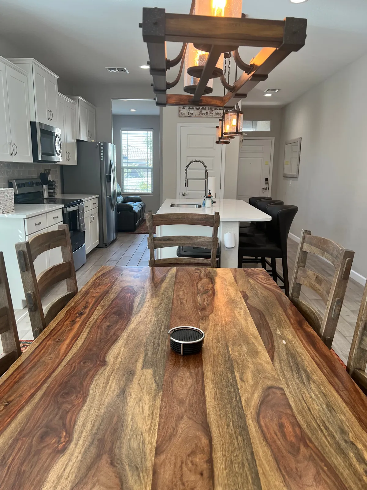 A welcoming dining area features a large table, elegant chandelier, kitchen island with granite countertops, and a cozy seating area. The setup is perfect for family meals, entertaining, and lively conversations.