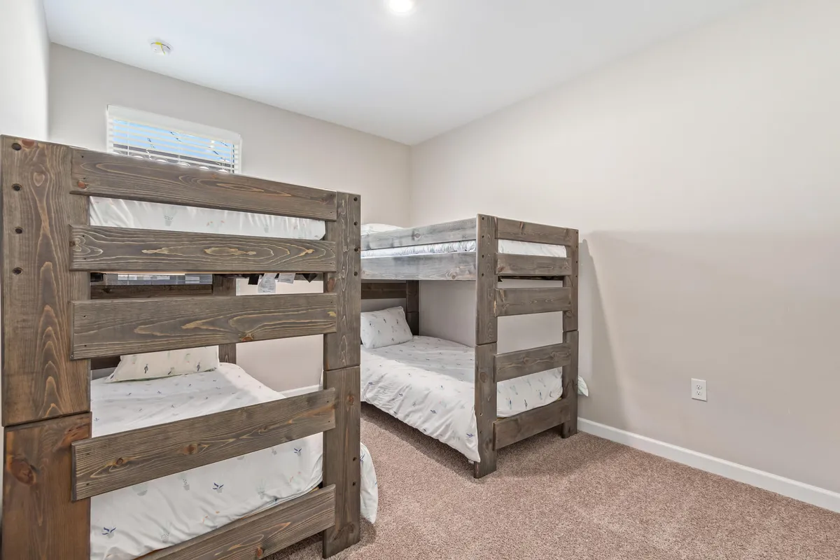 A playful bedroom with bunk beds, a wall-mounted window, and carpet flooring. The room is designed for both rest and fun, ideal for children or group stays.